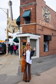 a woman standing in front of a building with a guitar hanging from the side of it