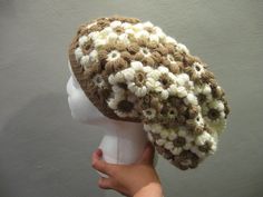 a person holding up a knitted hat on top of a mannequin head