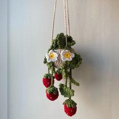 a crocheted hanging decoration with strawberries and daisies on the bottom, attached to a wall