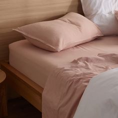 a bed with pink sheets and pillows on top of it next to a night stand