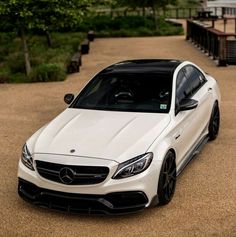 a white car parked on top of a parking lot next to a wooden bench and trees