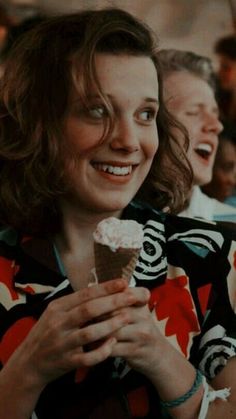 a woman eating an ice cream cone with other people in the background smiling and laughing