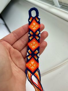 a hand holding an orange and blue beaded object