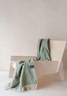 a green blanket sitting on top of a wooden bench in front of a white wall