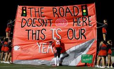 a group of cheerleaders standing in front of a large sign that reads the road doesn't here this is our year