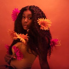 a woman with flowers in her hair posing for a photo against an orange background,