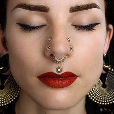 a woman with her nose piercing in gold and red lipstick, wearing large hoop earrings