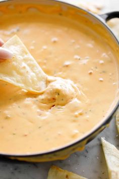 a person dipping tortilla chips into a pot of dip with cheese on the side