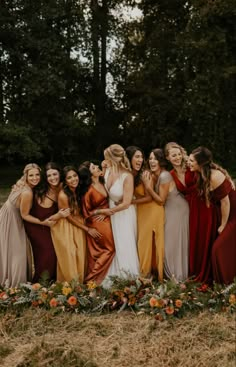 a group of women standing next to each other in front of trees and flowers on the ground