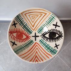 a ceramic bowl with an eye painted on the front and cross marks in the middle