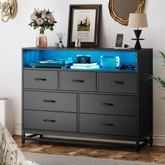 a black dresser with blue drawers and pictures on the top shelf, in front of a mirror