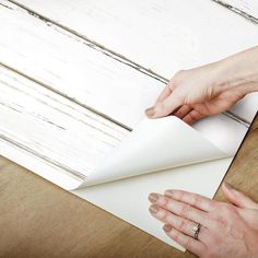 two hands are holding an envelope over a piece of paper on a wooden table with white paint