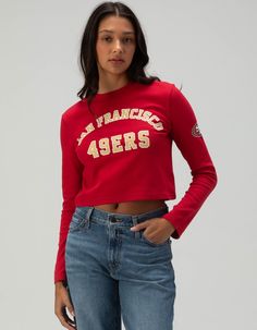 San Francisco 49ers Long Sleeve Baby Tee. Cheer On Your Team With This San Francisco 49ers Long Sleeve Baby Tee. Featuring "san Francisco 49ers" Screened Across The Front Chest And The Iconic Team Logo Graphic On The Left Sleeve, This Fitted Tee Offers Both Style And Team Spirit. Perfect For Game Day Or Casual Outings! 94% Cotton, 6% Spandex. Machine Wash. Imported. Model Is Wearing A Size Small. Model Measurements:height: 5'8" Bust: 32"waist: 24"hips: 35" | San Franscico 49ers Long Sleeve Baby Tee Womens 49ers Shirt, Throwback Fan Gear Tops For Fall, Throwback Long Sleeve Tops For Game Day, Throwback Tops For College Football Season, Team-colored Fitted Top For Game Day, Fitted Team-colored Tops For Game Day, Fitted Team Name Tops For Fans, Throwback Red College Top, Red Throwback Tops For Game Day