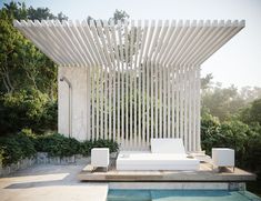 a white couch sitting on top of a wooden platform next to a swimming pool with trees in the background