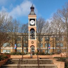 a clock tower in front of a building with steps leading up to it and trees on either side