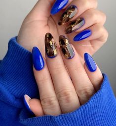 a woman's hand with blue and gold nail polishes on her nails,