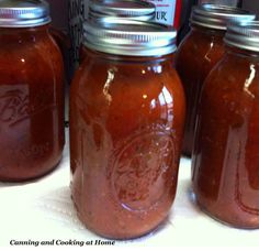 three jars filled with red sauce sitting on top of a white tablecloth covered counter