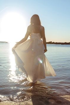 a woman in a white dress walking into the water