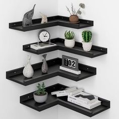 three black shelves with different types of plants and books on them, one shelf has an alarm clock