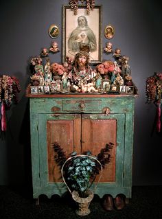 an old cabinet with many figurines and pictures on the top, sitting in front of a painting