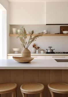 three stools sit in front of a counter top with a vase on it and bowls