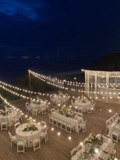 tables and chairs are set up on the deck for an outdoor dinner with string lights