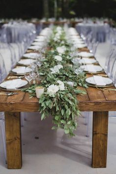 a long wooden table topped with white flowers and greenery