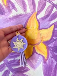 a hand holding a purple keychain with a yellow flower on the front and side