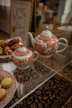 a glass table topped with red and white plates filled with pastries next to a teapot