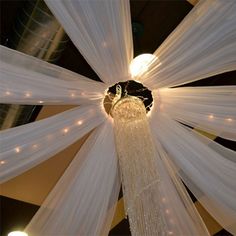 a chandelier hanging from the ceiling in a room with white drapes and lights