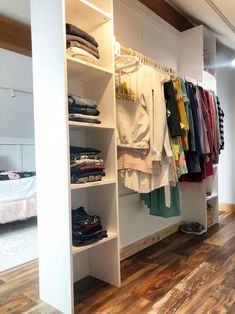 an open closet with clothes hanging on the wall and wooden flooring in front of it