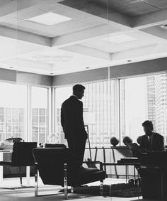 a man standing in an office looking out the window at other people working on their desks