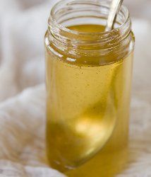 a jar filled with liquid sitting on top of a white blanket next to a spoon