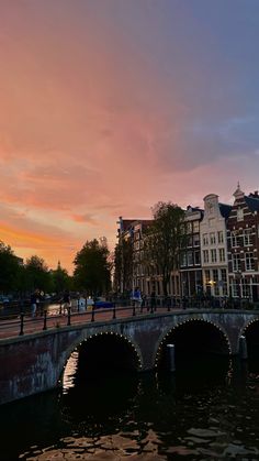 people are walking on the bridge over the water at sunset or dawn in an urban area