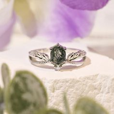 a close up of a ring on a white surface with purple flowers in the background