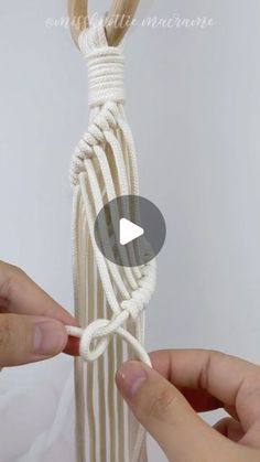 two hands are tying a white rope around a wooden pole and another hand is holding the string