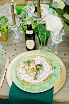 a table set with green and gold place settings, champagne glasses, candles and plates