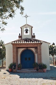 a small church with a blue door and bell on the top is surrounded by potted plants