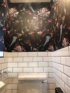 a white toilet sitting next to a black and white tiled wall with flowers on it