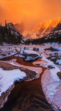 the sun is setting over a mountain valley with frozen water and snow on the ground