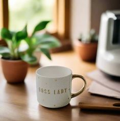 a coffee cup sitting on top of a wooden table next to a potted plant