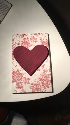 a card with a red heart on it sitting on a table next to a book