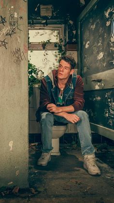 a man sitting on top of a toilet in a room with graffiti all over the walls