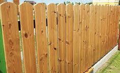 a wooden fence in the grass next to a green trash can and a yellow fire hydrant