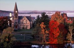 an old church surrounded by trees with fog in the sky behind it and water below