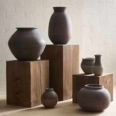 several vases are stacked on wooden blocks in front of a white brick wall and floor