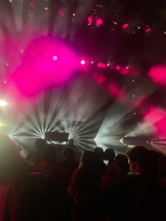 a crowd of people standing on top of a stage under bright colored lights and spotlights