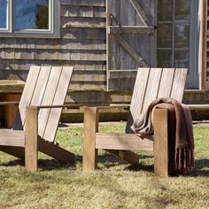 two wooden chairs sitting on top of a grass covered field next to a building with windows