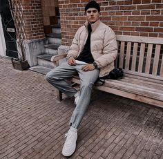 a man sitting on a bench in front of a brick building with his legs crossed