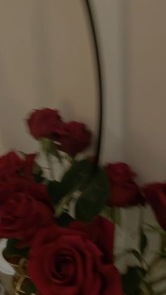 a vase filled with red roses sitting on top of a white table next to a mirror